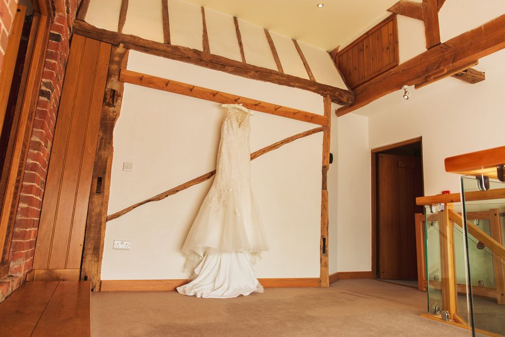A white wedding dress hangs elegantly against exposed wooden beams in a rustic room.