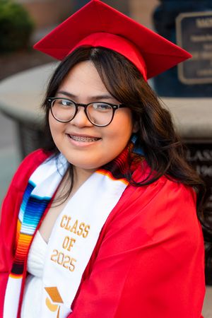 Graduate in bright red cap and gown with colorful stole smiles during graduation photo session.