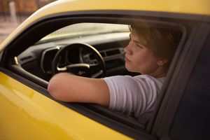A person adjusts the rearview mirror while sitting in the driver's seat of a yellow vehicle.
