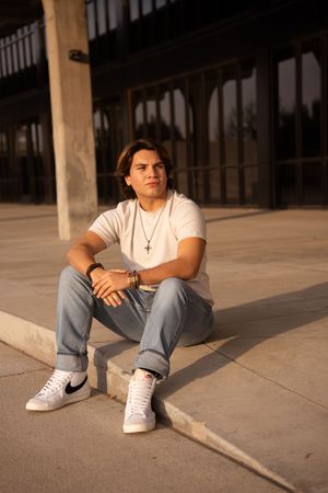 Person sitting on concrete floor wearing white t-shirt, jeans and white sneakers in artistic photo series.