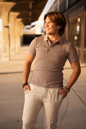 Person wearing a gray polo shirt and white pants stands in warm sunlight against a beige architectural backdrop.