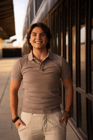 Person wearing a tan polo shirt and light colored pants stands in a hallway with wooden beams.