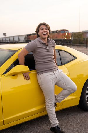 Person in casual wear posing playfully next to a bright yellow sports car on a rooftop parking area.