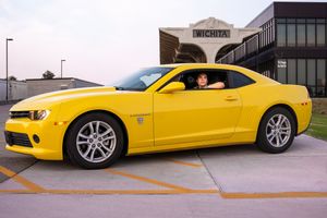A bright yellow Chevrolet Camaro SS sports car parked in front of a commercial building during sunset.