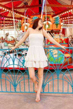 A sequence of carousel photos showing someone in a white dress posing playfully against a turquoise railing at a carnival.
