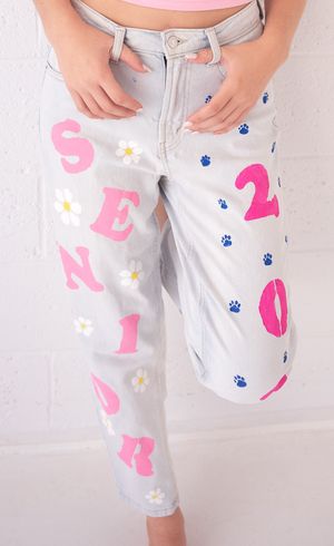 Light wash denim shorts decorated with pink letters, blue paw prints and white daisy flower designs.