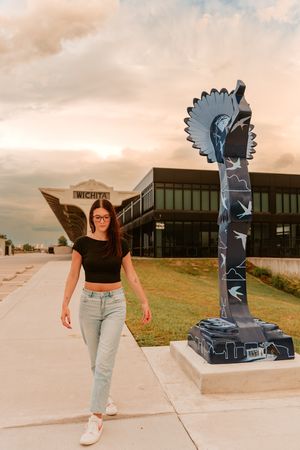 A modern sculpture of a geometric bird stands prominently against a sunset sky outside a commercial building.