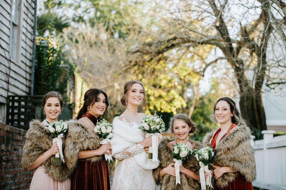 Wedding party poses together outdoors under trees in formal attire during an autumn celebration.