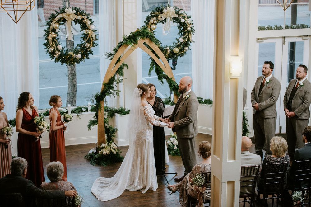 Wedding guests and bridal party gathered inside an elegant white room decorated with floral arrangements.