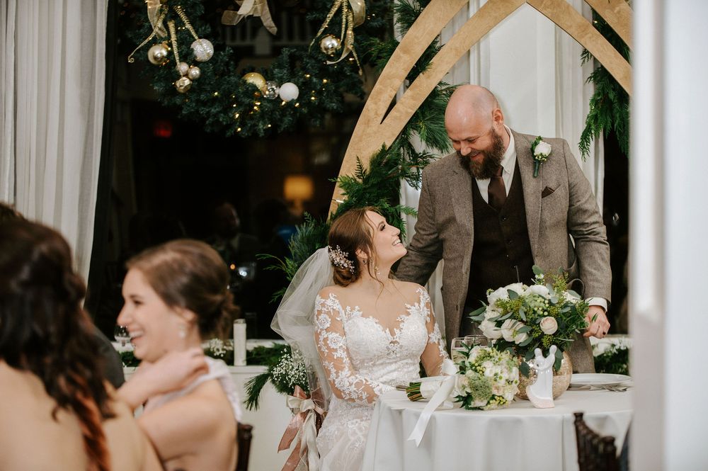 A couple shares a tender moment during their wedding reception while signing documents at a decorated table.