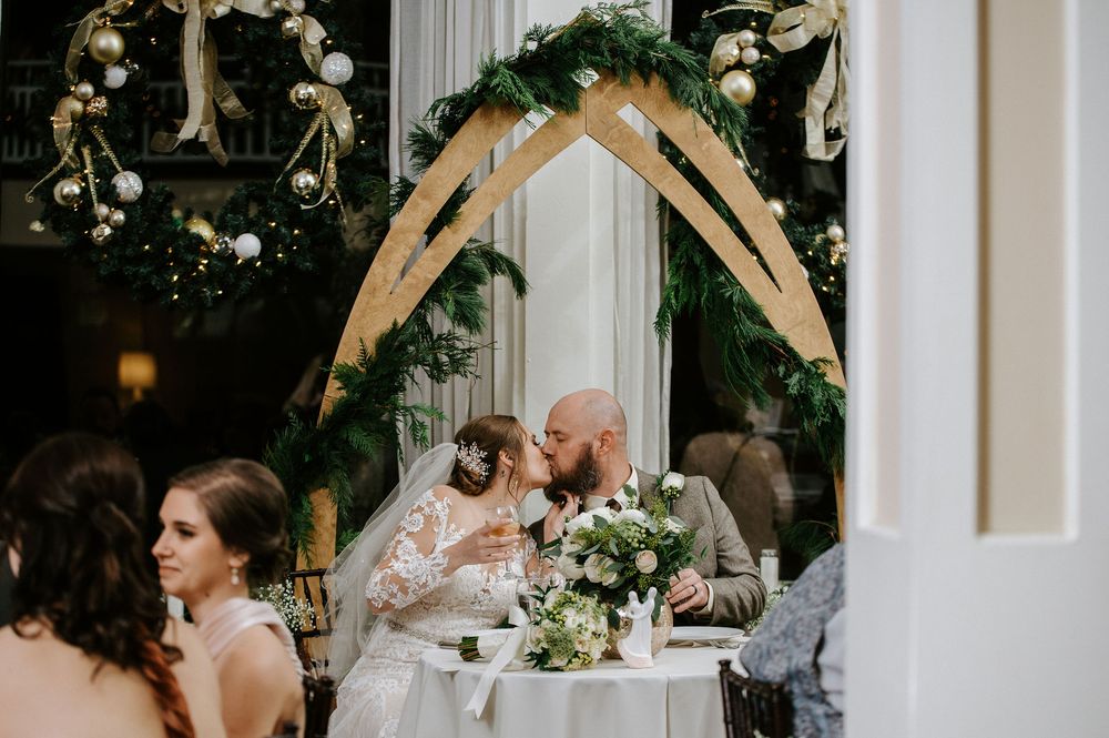 Wedding ceremony setup with white floral arch and greenery decorations in front of a white building.