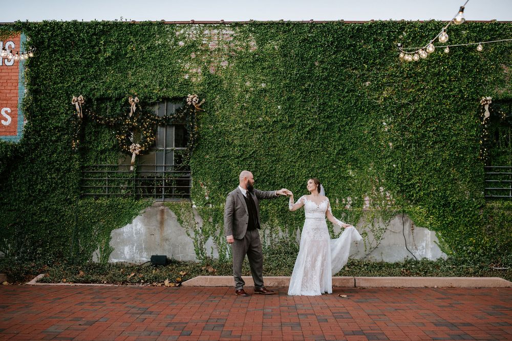 Wedding couple walks together through a lush garden courtyard with ivy covered walls.