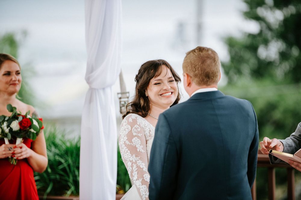 A joyful outdoor wedding ceremony under a white canopy with floral decorations and greenery in the background.