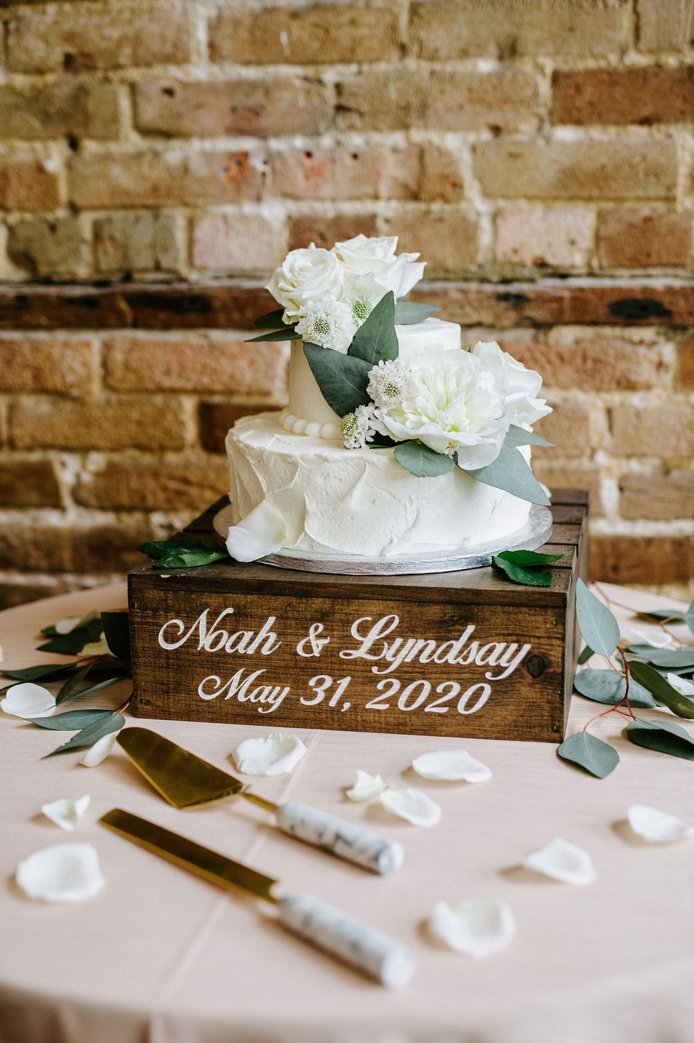 Rustic wooden wedding signs with white flowers and greenery displayed against a brick wall.