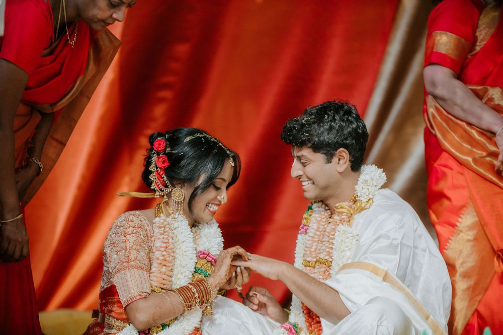 Wedding ceremony moment captured against a vibrant red backdrop with traditional Indian decorations.