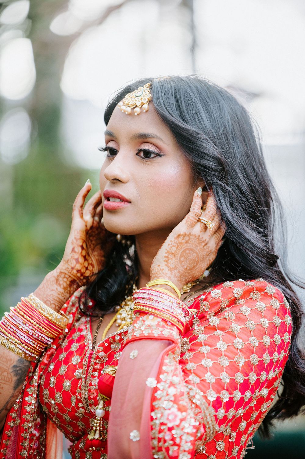 Bride in red and gold traditional Indian attire with henna adorned hands posing for portraits.