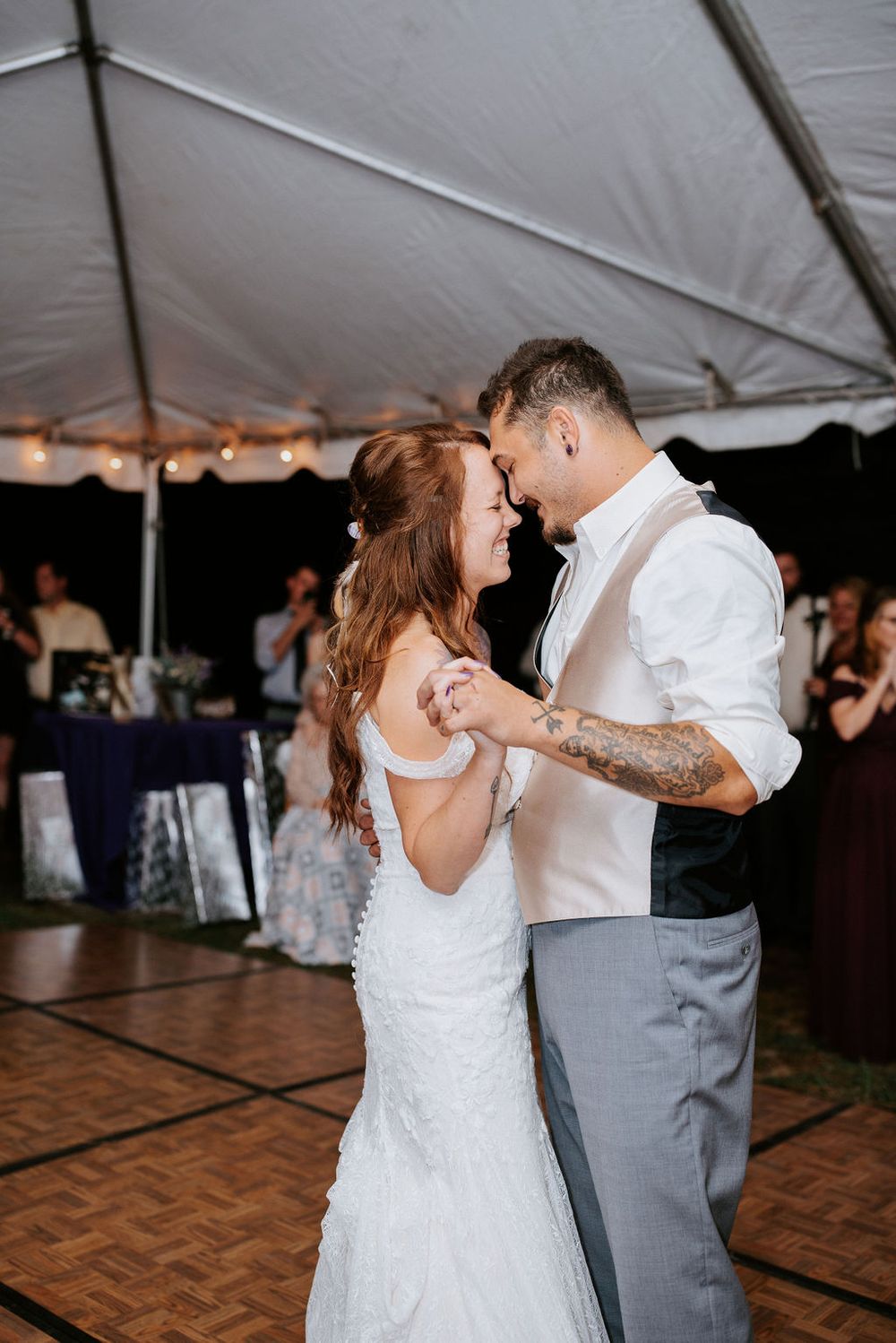 A couple shares a romantic dance moment under a white tent at their wedding reception.