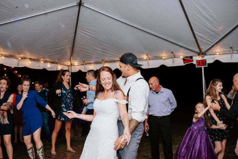 Guests dancing and celebrating under a white tent with string lights at a wedding reception.