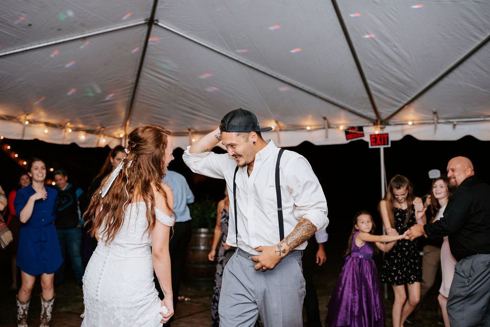 Wedding guests dancing and celebrating under a large white tent during an evening reception.