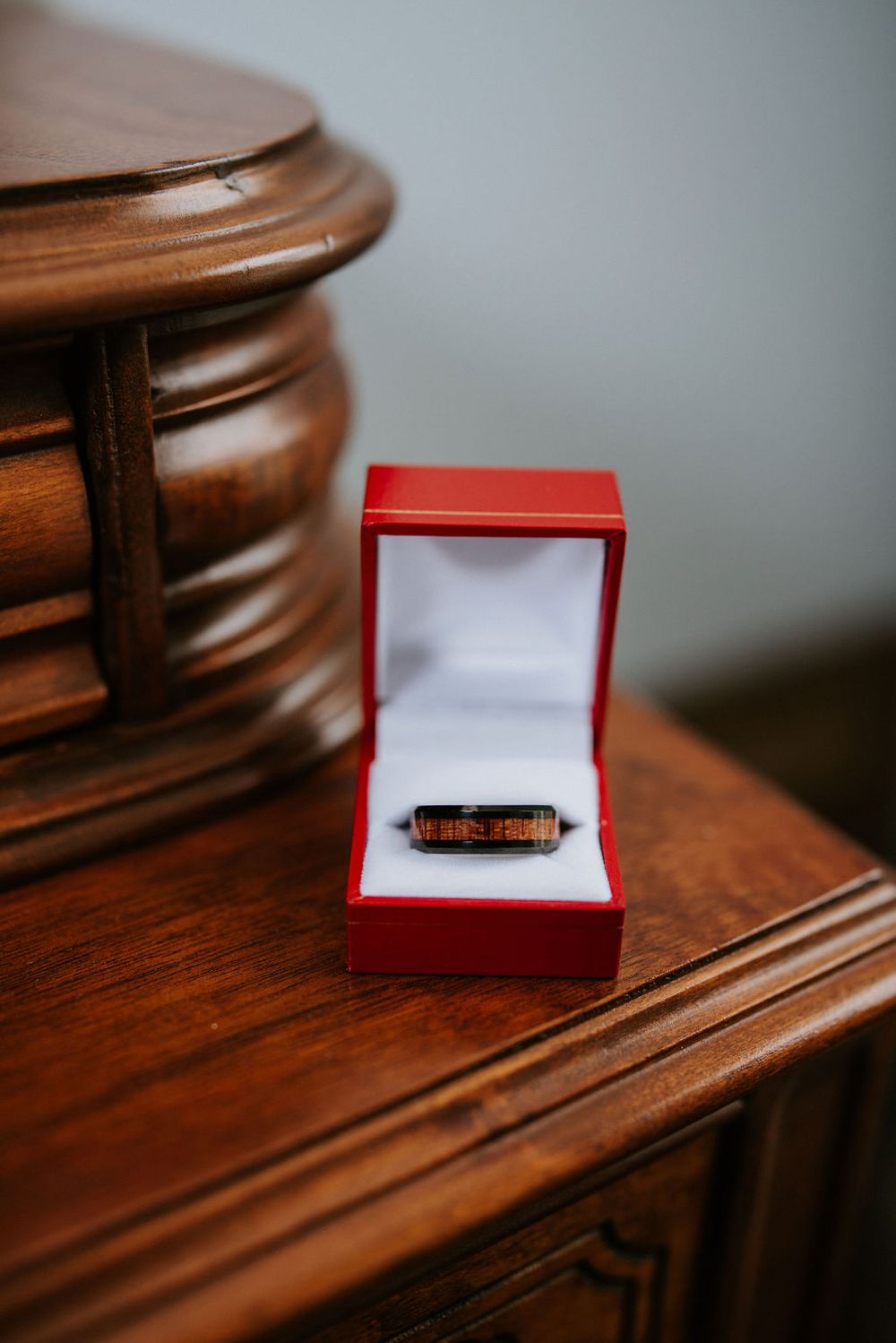 A small red jewelry box containing a ring sits on a polished wooden surface in natural light.