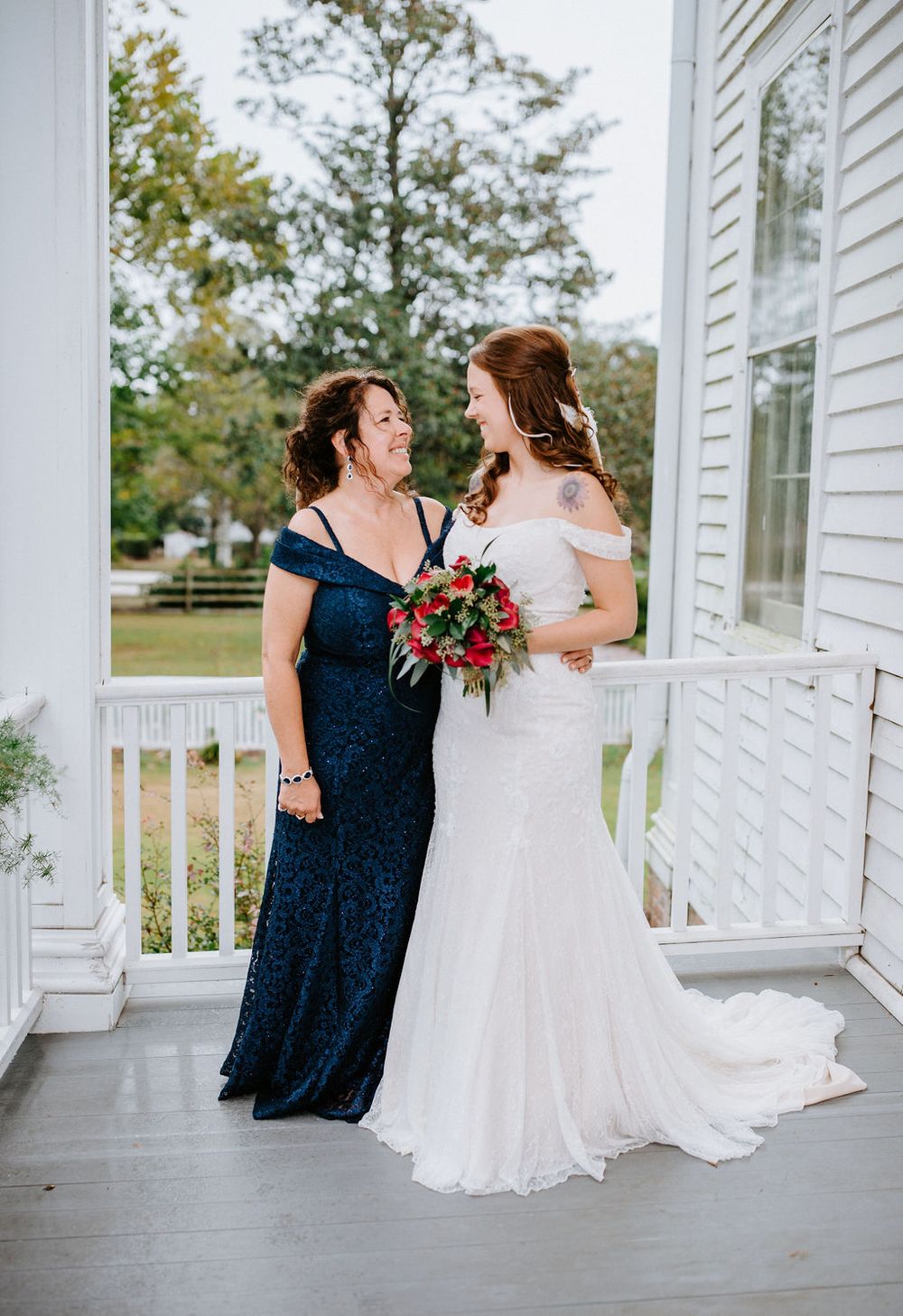 Wedding party members in navy blue and white dresses pose together on a white porch.