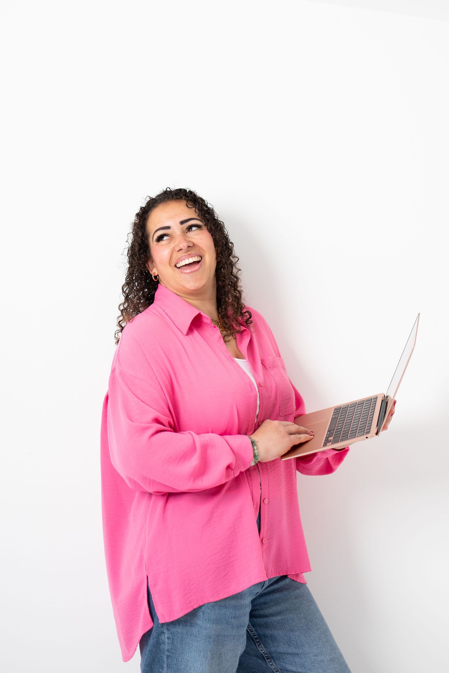 Smiling woman in pink shirt holding laptop against white background.