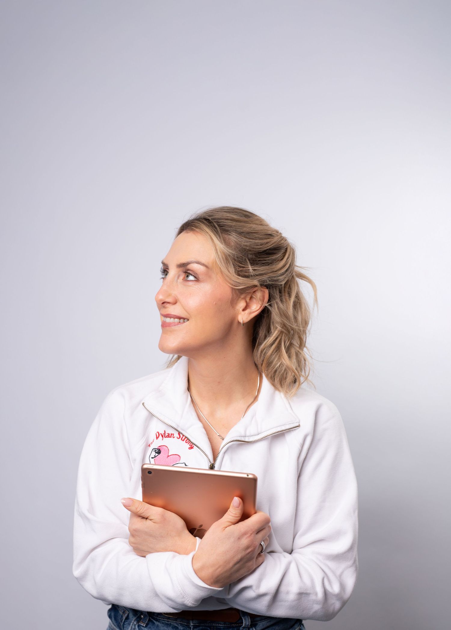 Healthcare professional in a white uniform jacket holding a tablet while looking to the side with a smile.