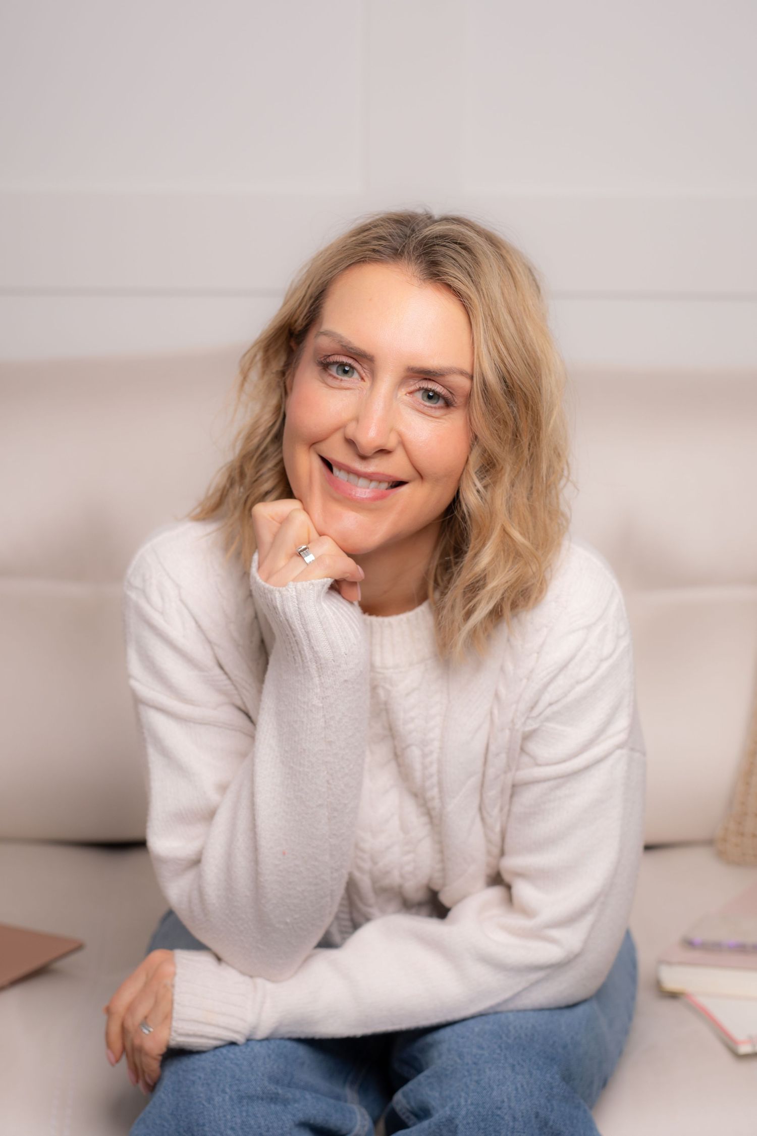 A person in a white sweater and jeans poses casually on a light-colored couch in a series of relaxed shots.