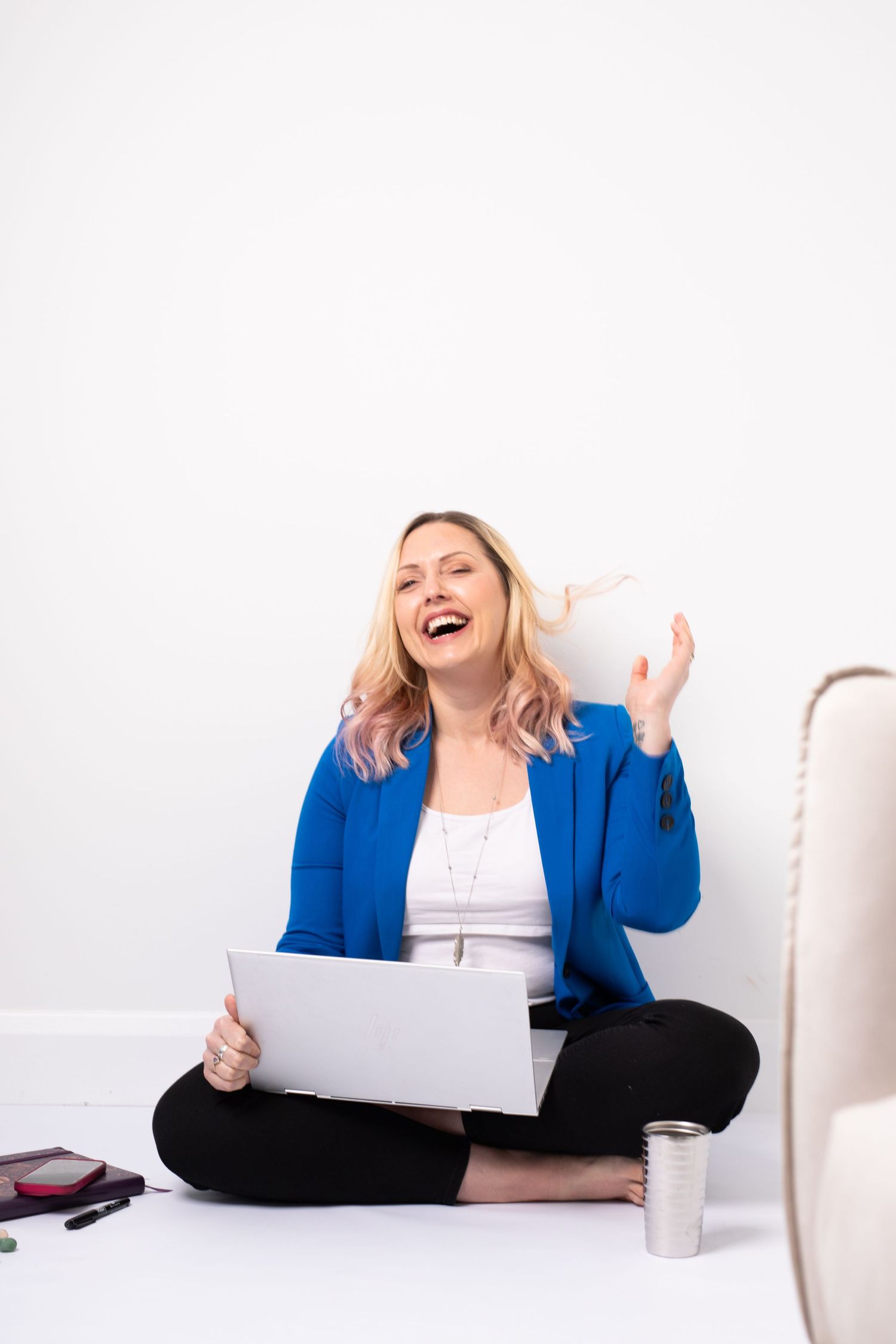 Professional in bright blue blazer sits cross-legged on floor with papers, expressing joy and celebration.