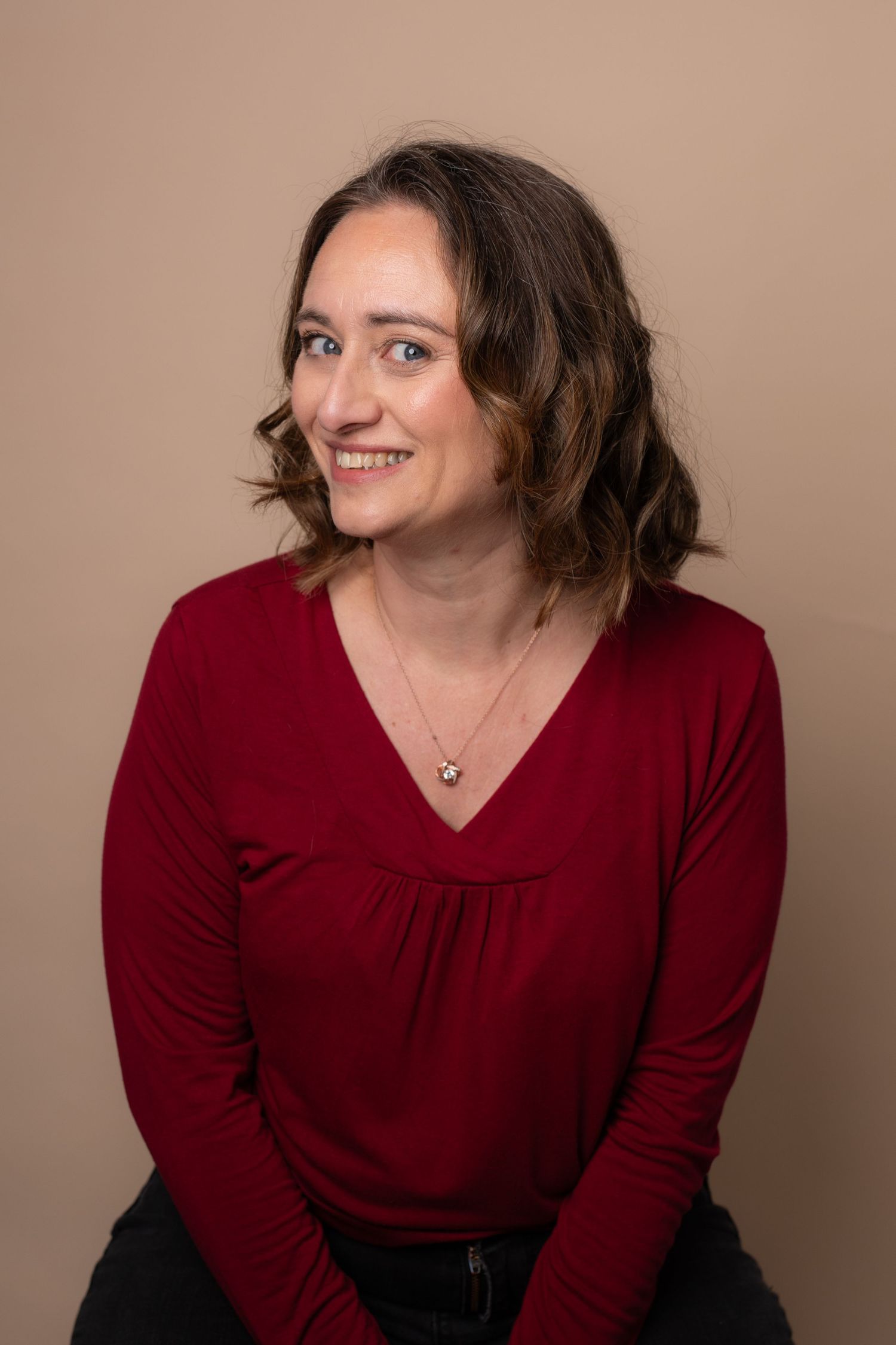 Professional portrait of someone wearing a burgundy v-neck sweater against a neutral background, smiling warmly.