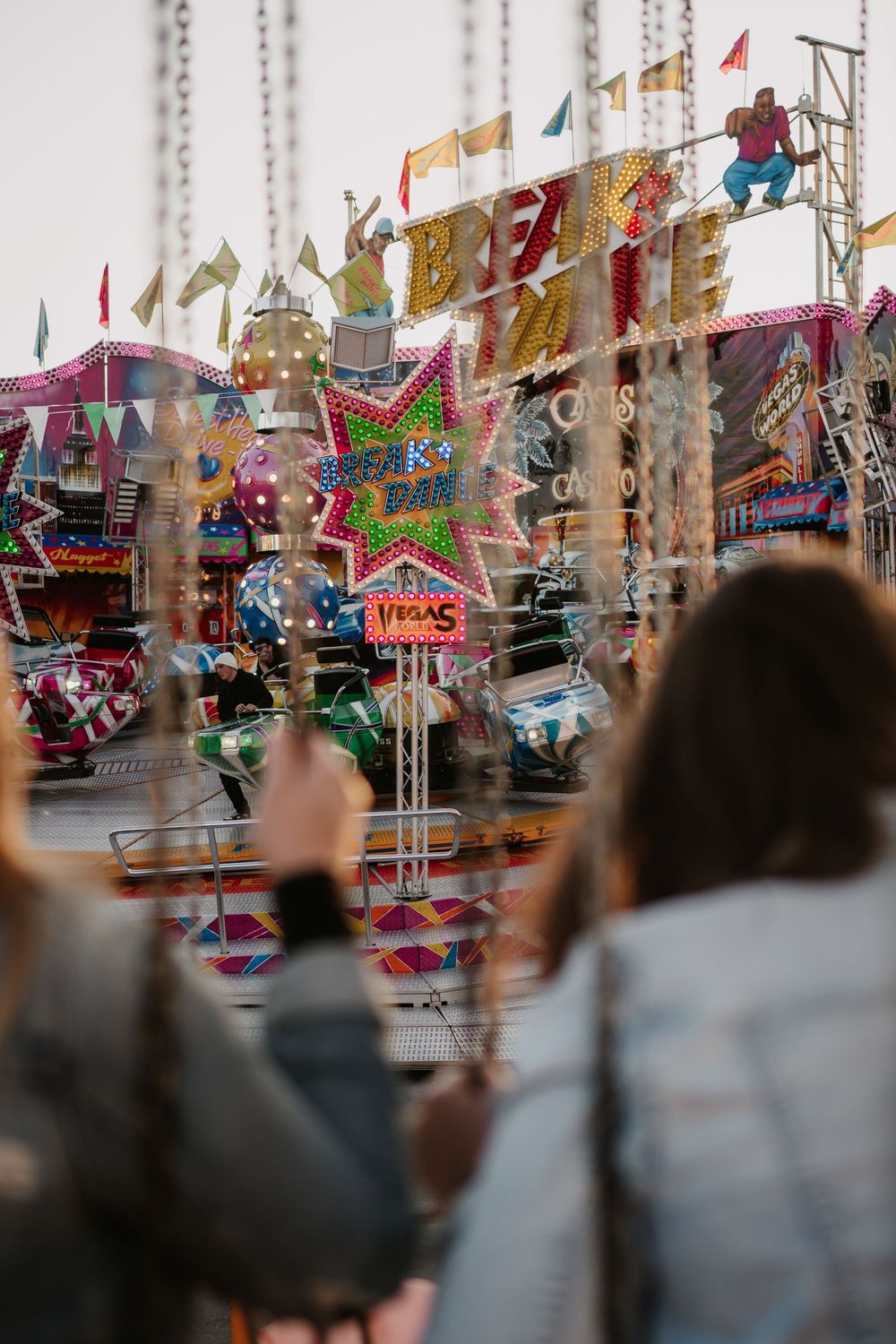 Colorful carnival rides and attractions with neon lights and flags create a festive atmosphere at a fairground.