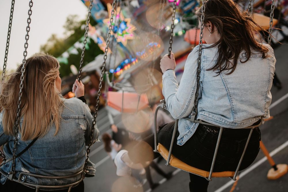 Person on carnival swing ride at dusk with colorful lights and decorations in the background.
