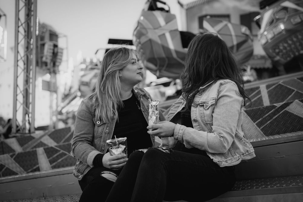 Two people laugh and enjoy drinks while sitting together at an outdoor carnival in black and white photography.