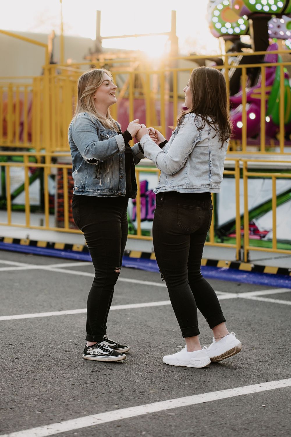 Two people in black pants and sneakers stand together on a playground surface during golden hour lighting.