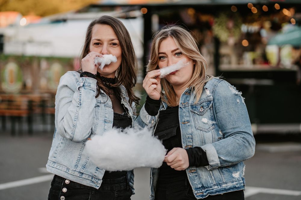 Two people share cotton candy at a carnival while wearing denim jackets on a festive evening.