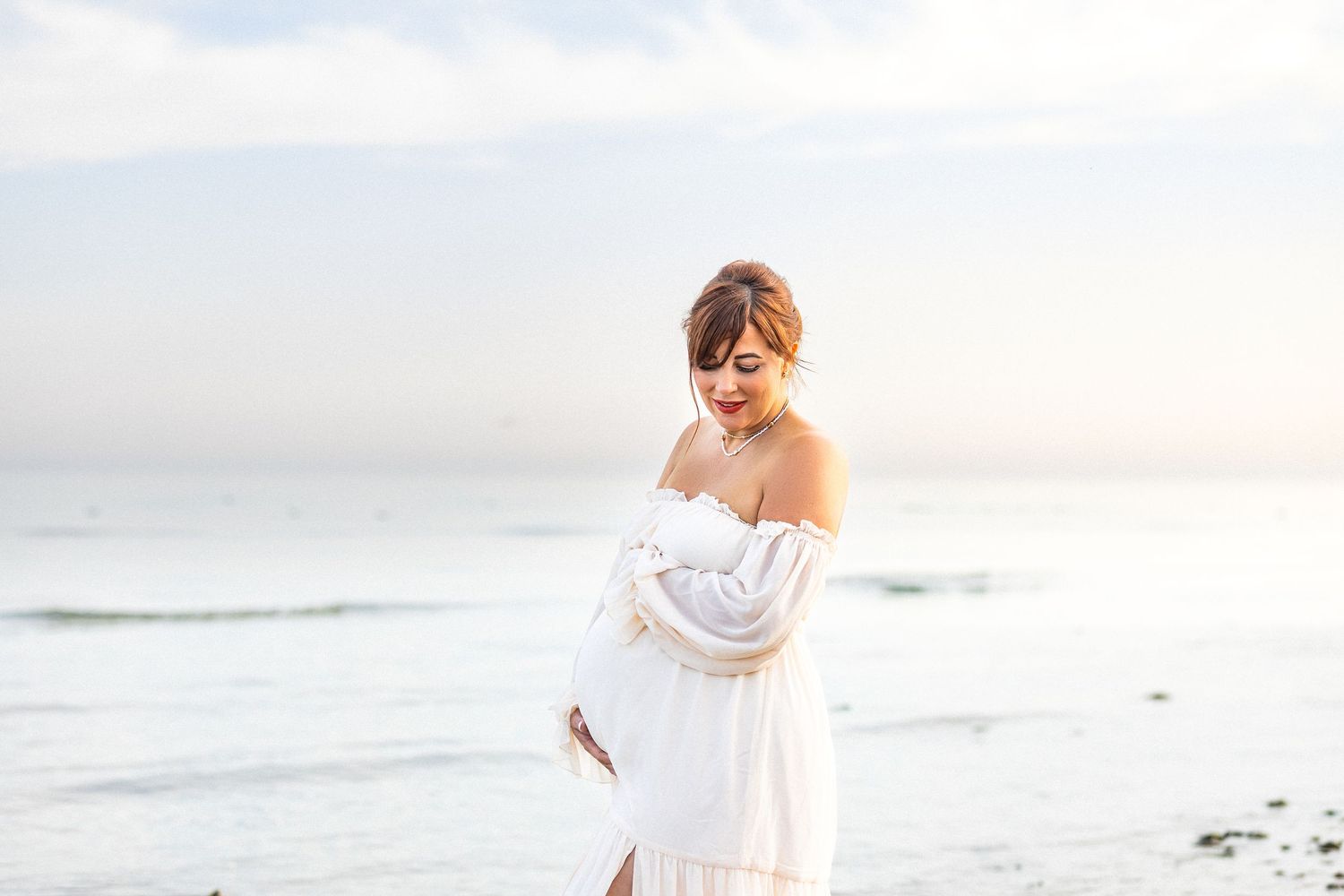 A person in a flowing white dress walks along a misty beach at sunset creating a dreamy coastal scene.