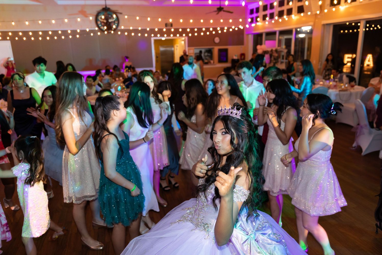 Crowded dance floor at a formal event with colorful purple and pink lighting creating a festive atmosphere.