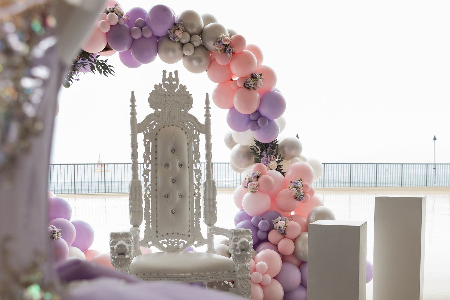 Elegant wedding arch decorated with pink and purple balloons and flowers in a bright indoor venue.