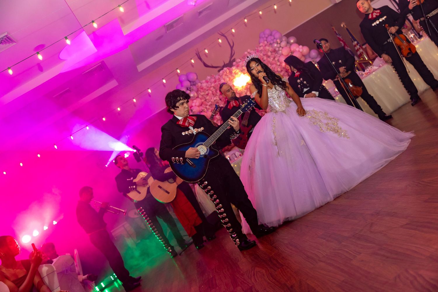 People dancing at a wedding reception under vibrant pink and green lighting on a wooden dance floor.