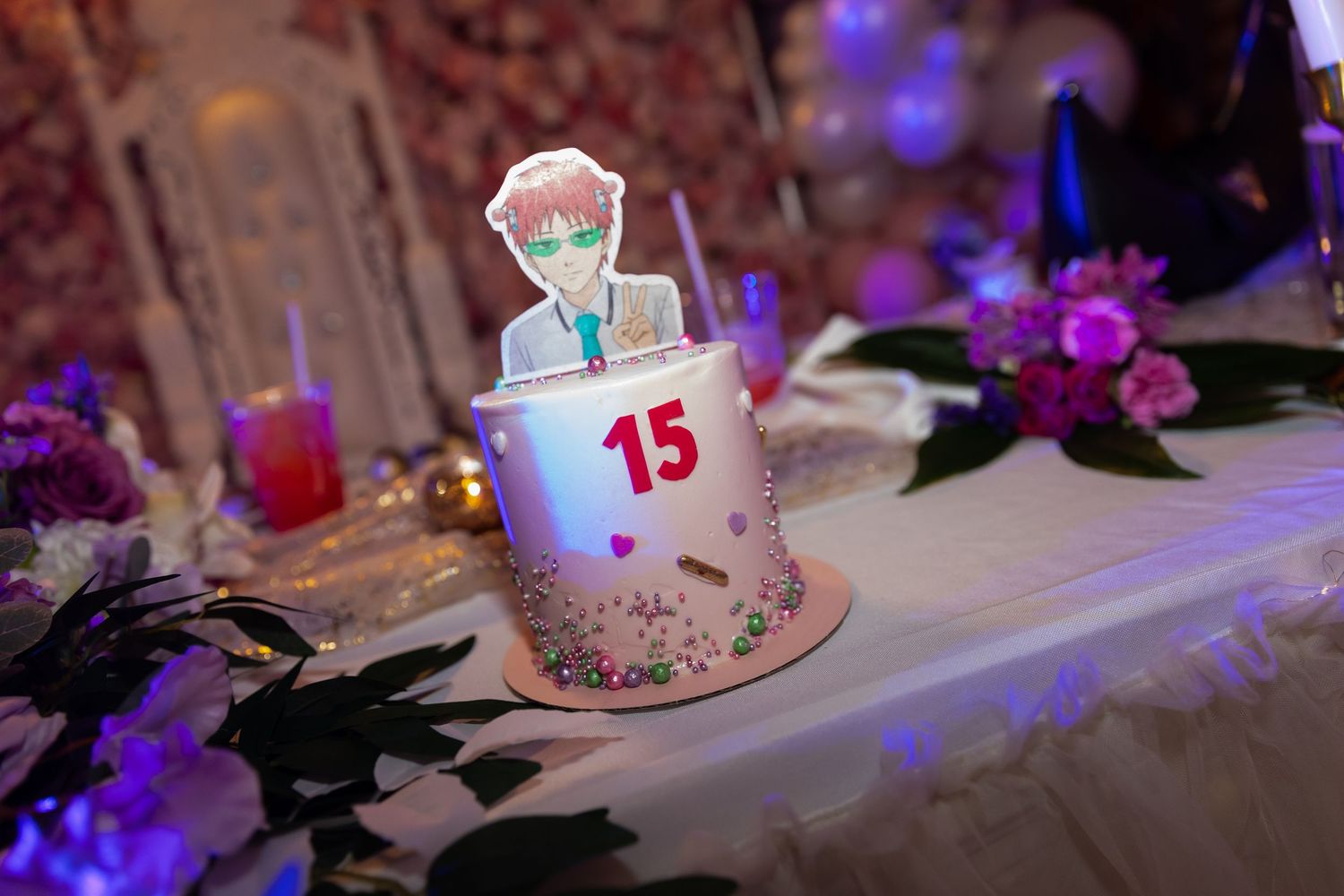 A decorated birthday cake with sparklers and purple lighting creates a festive party atmosphere on a white tablecloth.