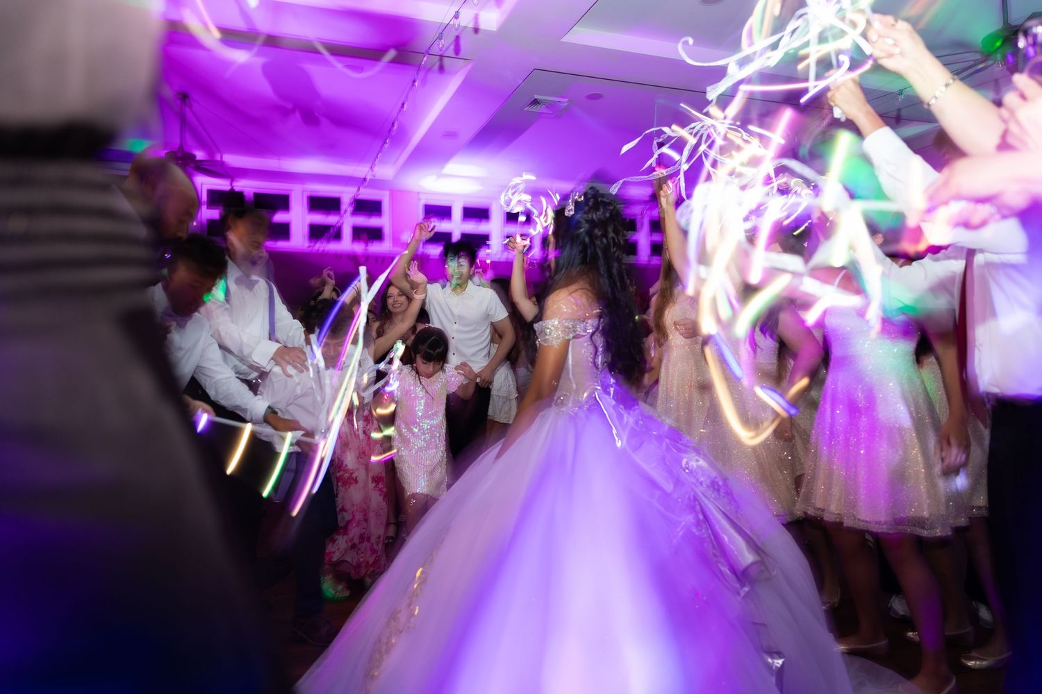 Motion-blurred dance floor scene at a wedding reception with purple lighting and glowing light trails.