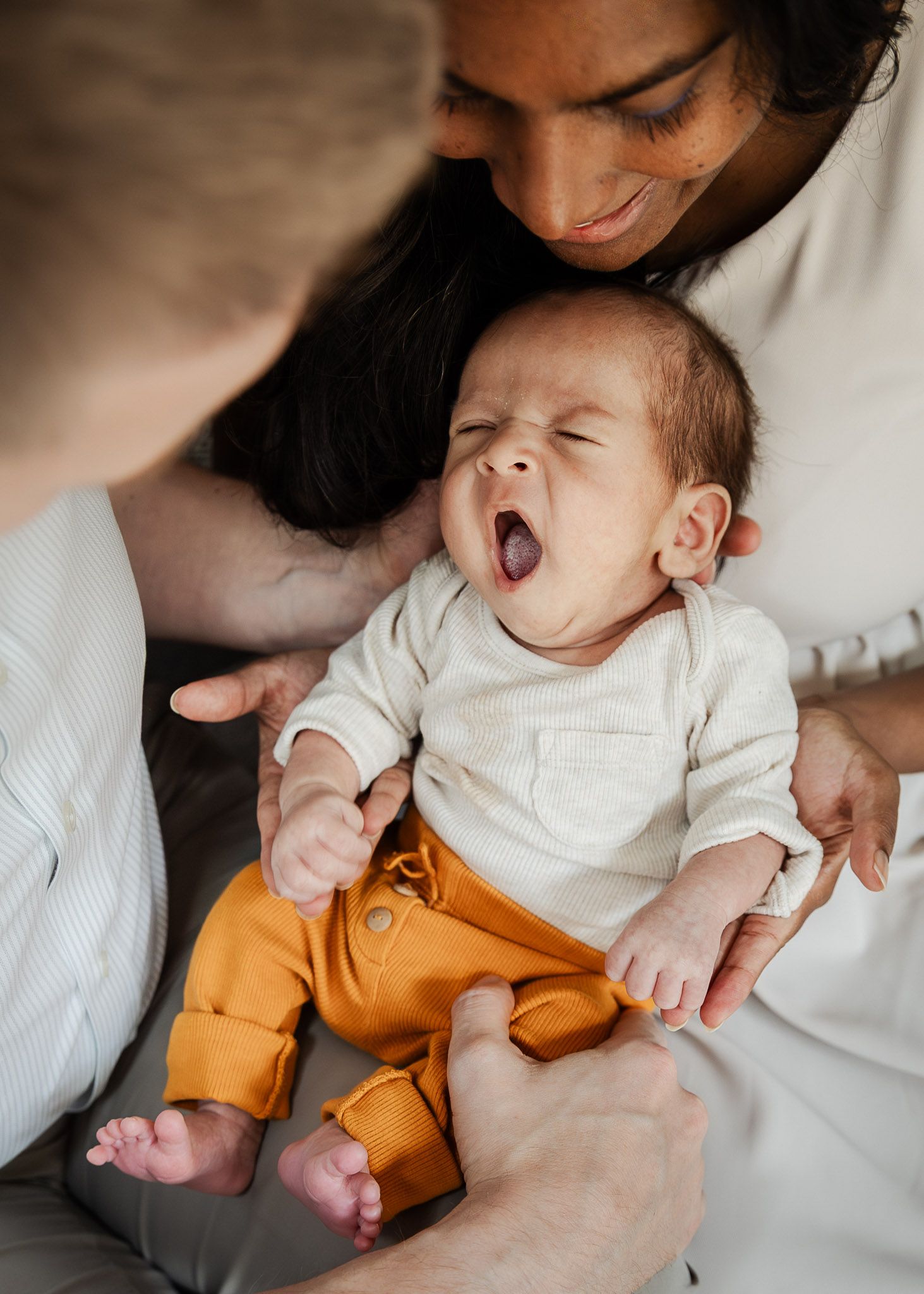 A newborn baby yawns as his parents hold him during a relaxed in-home photoshoot in Bristol with Little Bodhi Photography