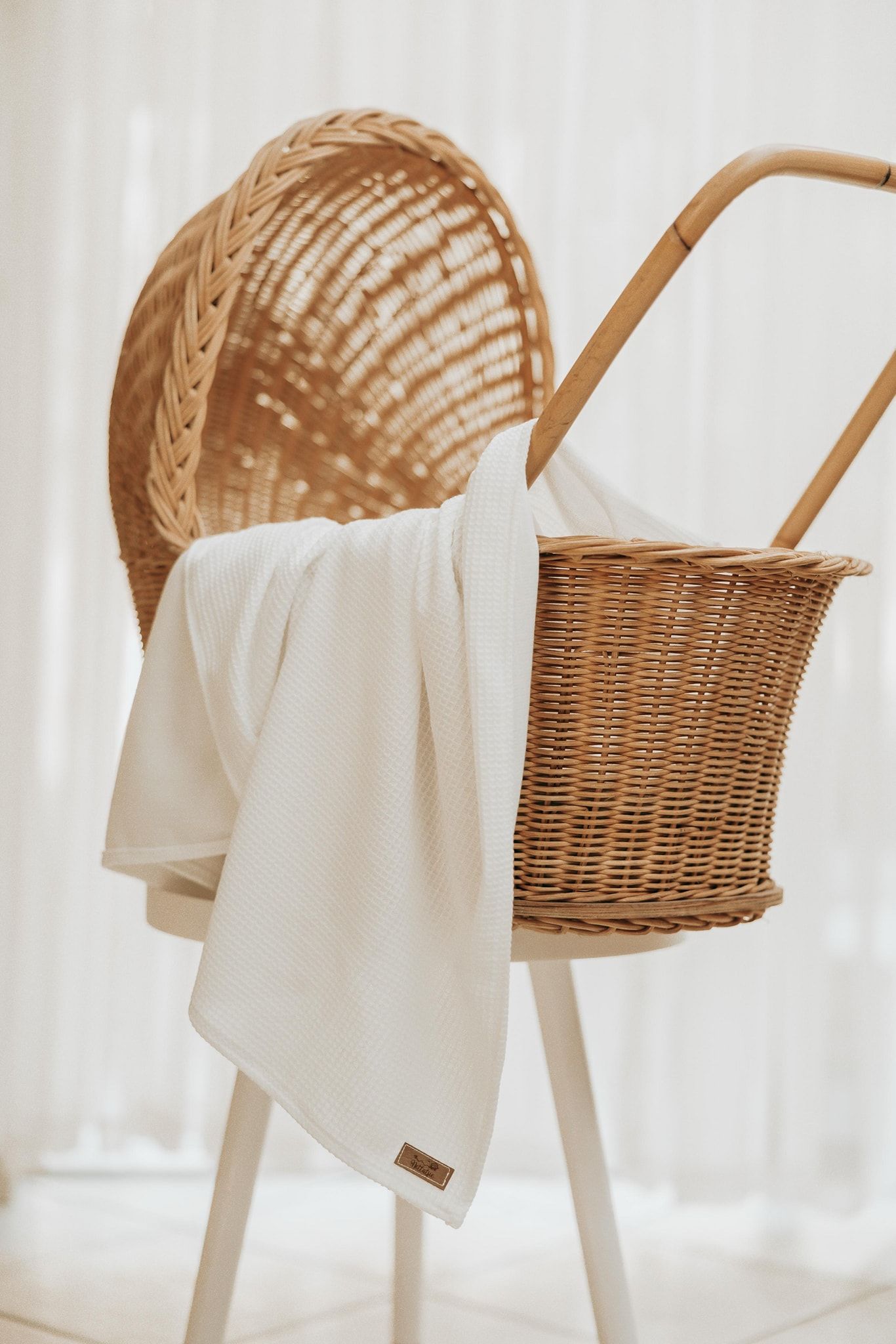 A woven wicker basket with white fabric draped over it sits on a white chair in soft natural lighting.