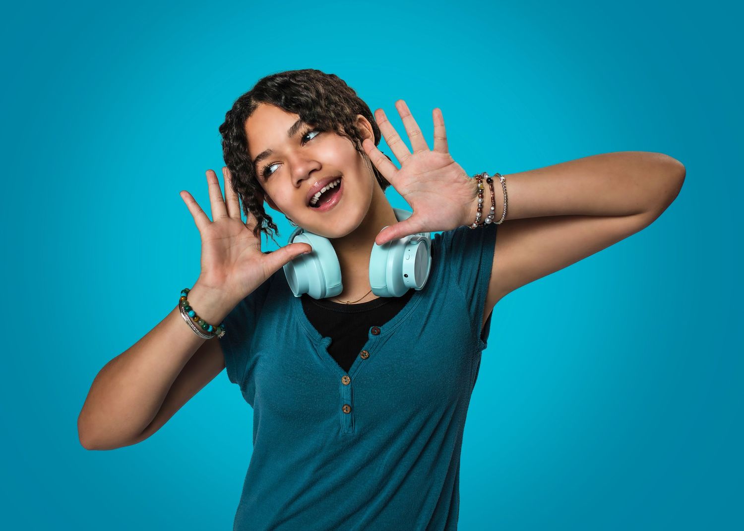 A senior graduate in teal shirt making playful expressions and poses against turquoise background in photo sequence for personality portrait