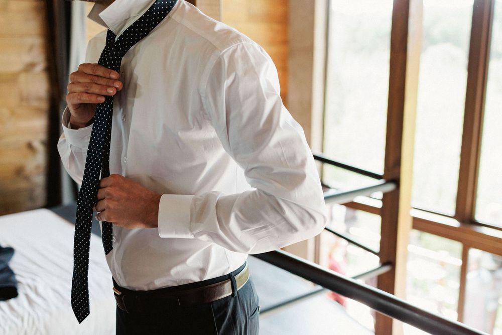 Groom adjusting his tie while friends laugh nearby
