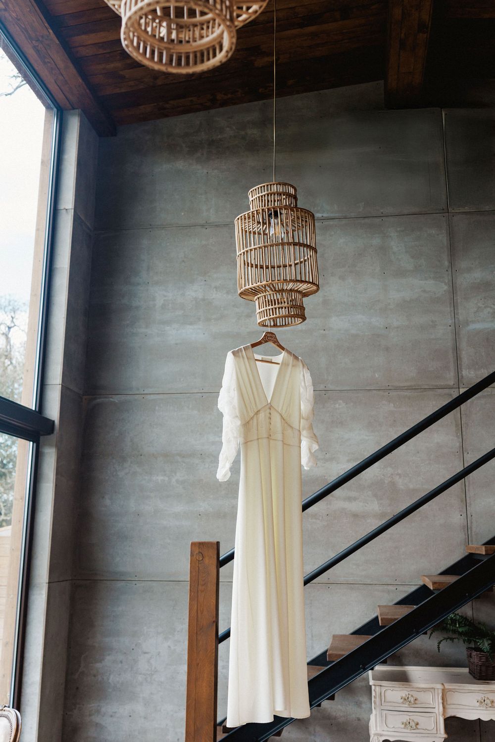 Elegant cream-colored wedding dress hanging from bamboo chandelier against concrete wall in Herdade do moinho novo bungalows
