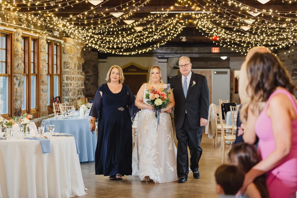 Wedding party dancing and celebrating under twinkling string lights in an elegant indoor reception venue.
