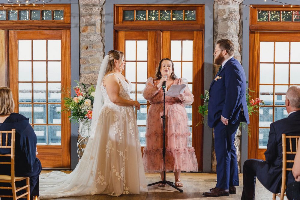 A wedding party gathers in a rustic room with stone walls and large windows overlooking a scenic view.