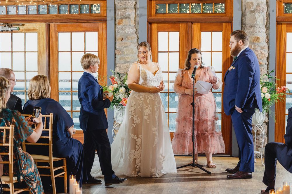 Wedding guests dancing and socializing during a reception in a rustic venue with large windows and wooden beams.