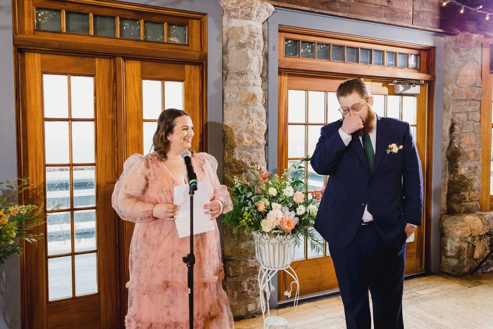 Wedding party stands in front of rustic stone walls and large windows at a mountain venue.